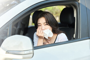 Young Woman Feeling Sick and Covering Mouth with Tissue in Car Interior on Sunny Day