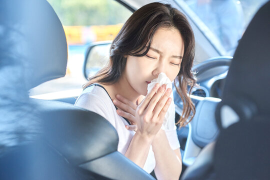 Young Woman Feeling Sick and Covering Mouth with Tissue in Car Interior on Sunny Day