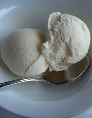 Delicious Vanilla Ice Cream Scoops in a White Bowl with Silver Spoon, on a soft fabric surface