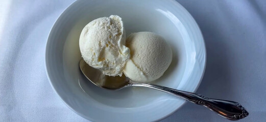 Delicious Vanilla Ice Cream Scoops in a White Bowl with Silver Spoon, on a soft fabric surface