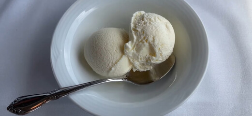 Delicious Vanilla Ice Cream Scoops in a White Bowl with Silver Spoon, on a soft fabric surface