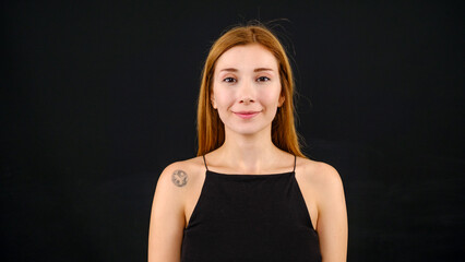 A chest-up headshot of a young, brown-haired woman taken in a studio setting with a black background