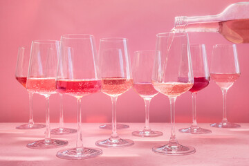 Rose wine poured from a bottle into a glass at a wine tasting, side view on a pink background