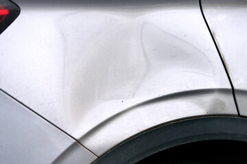 Dented, scratched car body near rear wheel arch showing paint damage, huge deformation from exterior impact. Rear side of vehicle fender panel with including deep dent, paint scratch. Selective focus