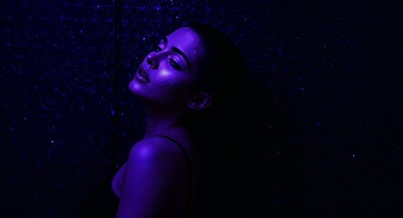 Seductive woman with shaved sides and purple glowing face paint posing against steel wall covered in digital code
