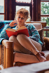 Obraz premium Attractive woman in her 40s spending peaceful time alone in a cozy mountain chalet. Enjoying moments of calm, comfort and reflection while relaxing indoors with books, technology or simply herself
