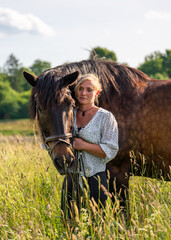 Beautiful rider gently strokes her brown horse in green field, sharing quiet moment of affection...