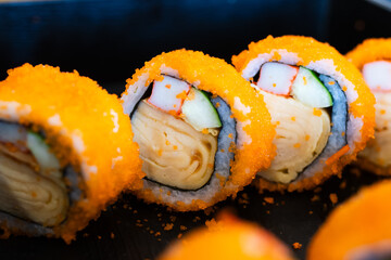 Sushi rolls filled with tamago, imitation crab, and cucumber, wrapped in seaweed and rice, coated with orange tobiko on the outside.