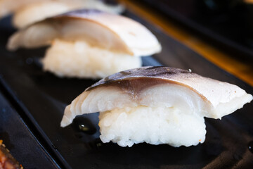 Saba nigiri sushi with a slice of grilled mackerel on top of vinegared rice, served on a black plate in a Japanese restaurant.