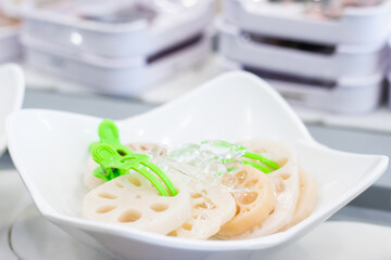 Fresh sliced lotus root served on ice in a white bowl, with green tongs, ready for hot pot or salad in an Asian-style buffet restaurant.