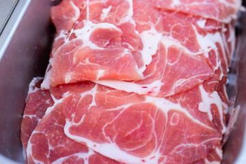 Fresh slices of raw pork neatly stacked in a stainless steel tray, ready for hot pot, shabu-shabu, or grilling at a buffet restaurant.
