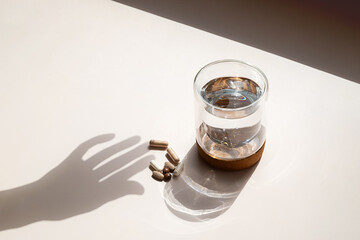 Various Capsules and Glass of Water with Hand Shadow on Light Background. Daily Vitamins and Pills...