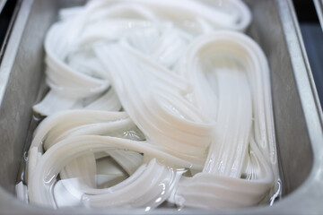 Fresh white flat rice noodles soaked in water, stored in a stainless steel tray for use in Asian hot pot, soup, or stir-fry dishes.