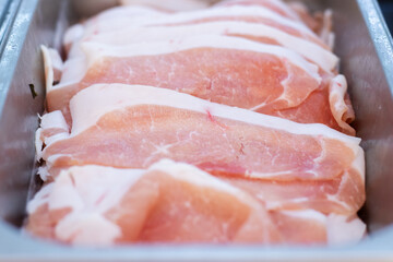 Thin slices of raw pork belly arranged in a stainless steel tray, ready for hot pot, barbecue, or shabu-shabu cooking at a restaurant or buffet.