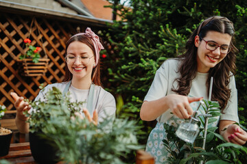 Two female friends or sisters taking care of plants with water can and mister	
