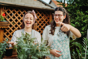 Two female friends or sisters taking care of plants with water can and mister	
