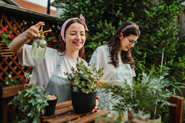 Two female friends or sisters taking care of plants with water can and mister	
