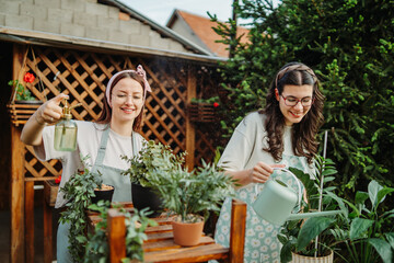Two female friends or sisters taking care of plants with water can and mister	
