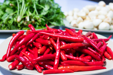 A plate full of fresh red chili peppers with coriander and garlic in the background, commonly used in Asian cooking for bold and spicy flavors.