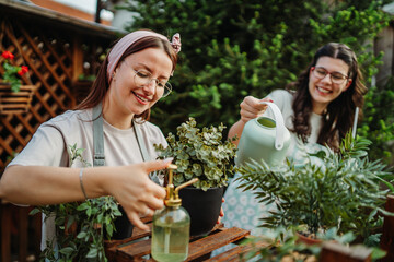 Two female friends or sisters taking care of plants with water can and mister	
