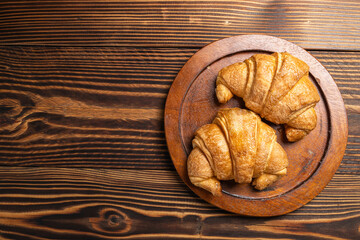 Freshly baked croissants on a wooden tray with a wooden background. Top view