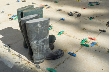 Pair of tall black rubber boots on newly laid tiles with clips and wedges, concept of construction,...