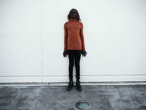 South Sudanese man wearing orange turtleneck in front of a blank wall