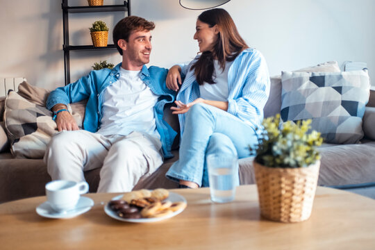 Young couple sitting on the sofa, smiling and talking peacefully together. Sharing dreams, planning their future, discussing marriage, children, or simply enjoying a quiet and loving moment at home - Powered by Adobe
