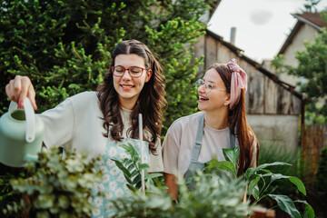 Two female friends or sisters taking care of plants with water can and mister	
