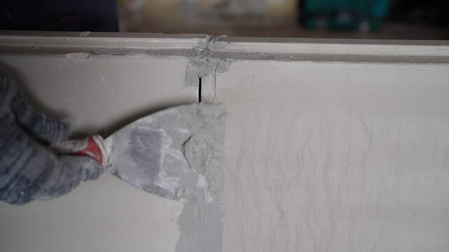 Construction worker carefully repairing wall crack using putty knife, smoothing surface with professional skill during home improvement project