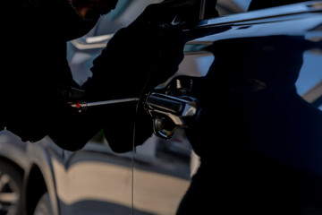 Criminal attempting to break into a parked car, highlighting risks of vehicle theft and security...