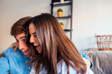 Young couple sitting on the sofa laughing together while watching something entertaining off screen. A joyful and relaxed moment of shared free time, using technology to enjoy each other's company