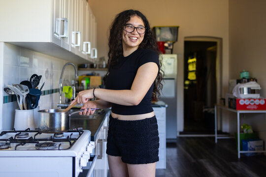 teen girl in kitchen stirring saucepan on stove