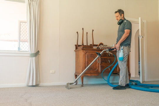 Male carpet cleaning professional using steam cleaner in home