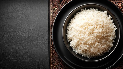 A black bowl filled with fluffy white rice atop a dark plate on a stylish patterned placemat against a contrasting black background for culinary aesthetics