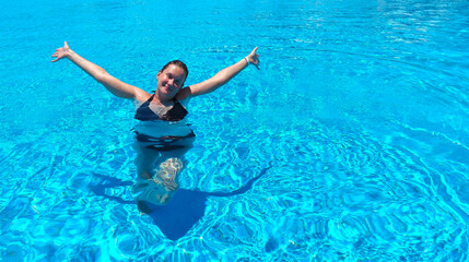 Young woman with arms outstretched enjoys swimming in a pool with clear blue water. Summer vacation, travel and relaxation concept