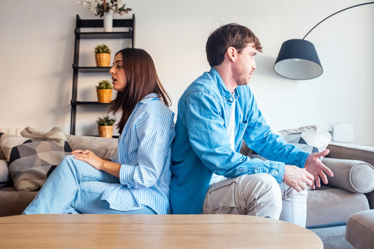 Young couple sitting back to back on the sofa after a serious argument, facing emotional tension and relationship issues. A moment of silence, disconnection, and reflection about their future together