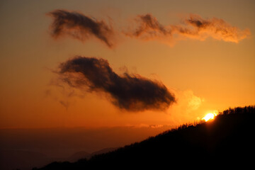Obraz premium Orange and red clouds paint the sky during beautiful mountain and forest sunsets and sunrises