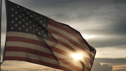 Close up USA American flag waving in the sky against sunset, sunrise outside background. Concept...