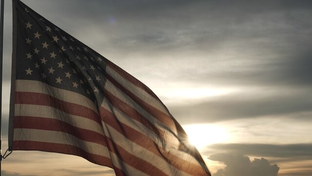 Close up USA American flag waving in the sky against sunset, sunrise outside background. Concept Fourth of July, 4th of July, Independence Day, Veteran Day, Holiday, Celebration. Freedom, Celebration