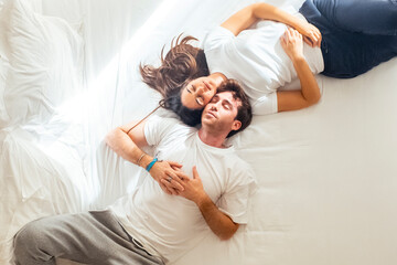 Young couple lying on the bed in casual homewear, smiling and talking about their future together....