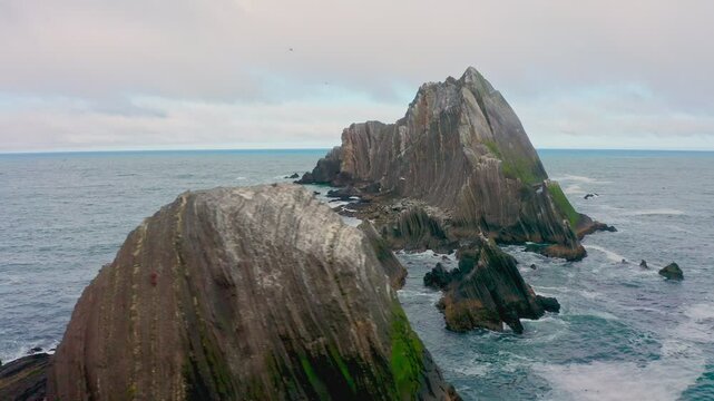 Aerial view of San Pedro Rock near Pacifica, California, along Highway 1. Rugged sea cliffs rise from the Pacific Ocean as waves crash beneath a dramatic coastal sky