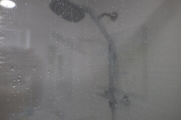 shower glass covered with water droplets with a blurred view of the shower in the background creating a soft atmospheric close up of a bathroom scene