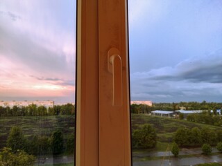 Fototapeta premium view through a window at sunset with moody sky and soft sunlight reflection, symbolizing contrast, duality, weather change, home comfort, perspective, architecture, lifestyle, real estate visuals