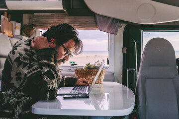 Mature man working remotely from inside a camper van, focused on his laptop while enjoying the...