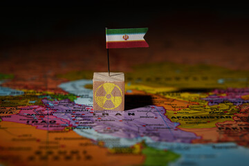 Iran flag pin on map with nuclear symbol block, representing nuclear issue or global tension.