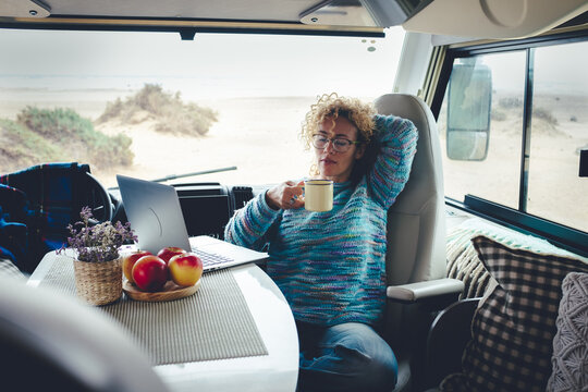Modern woman working remotely from inside a stylish camper van, using laptop and smartphone while traveling full-time. Digital nomad lifestyle combining freedom, technology, mobility and remote work