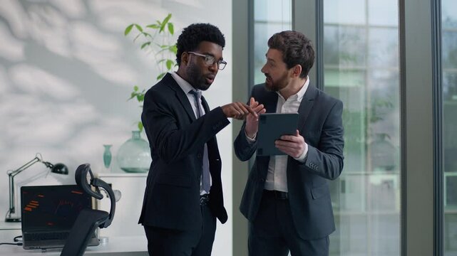 Two diversity multiethnic business men colleagues discuss online success looking in digital tablet computer amazed with good news multiracial businessmen males talking in office about startup growth - Powered by Adobe