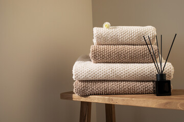 Stack of towels in neutral colors and aroma diffuser in modern aesthetic interior. Fabric bathroom accessories for hygiene, spa and skin care.