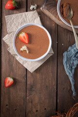 A smooth chocolate mousse in a white bowl, adorned with a fresh strawberry and delicate white...